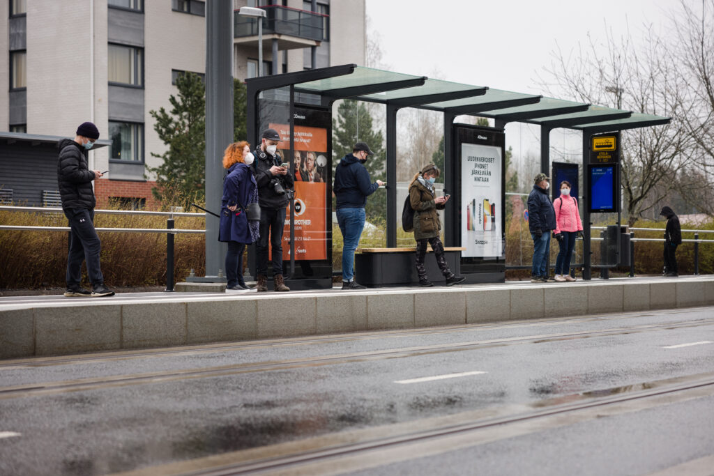 Ihmisiä Ratikan pysäkkikatoksen alla